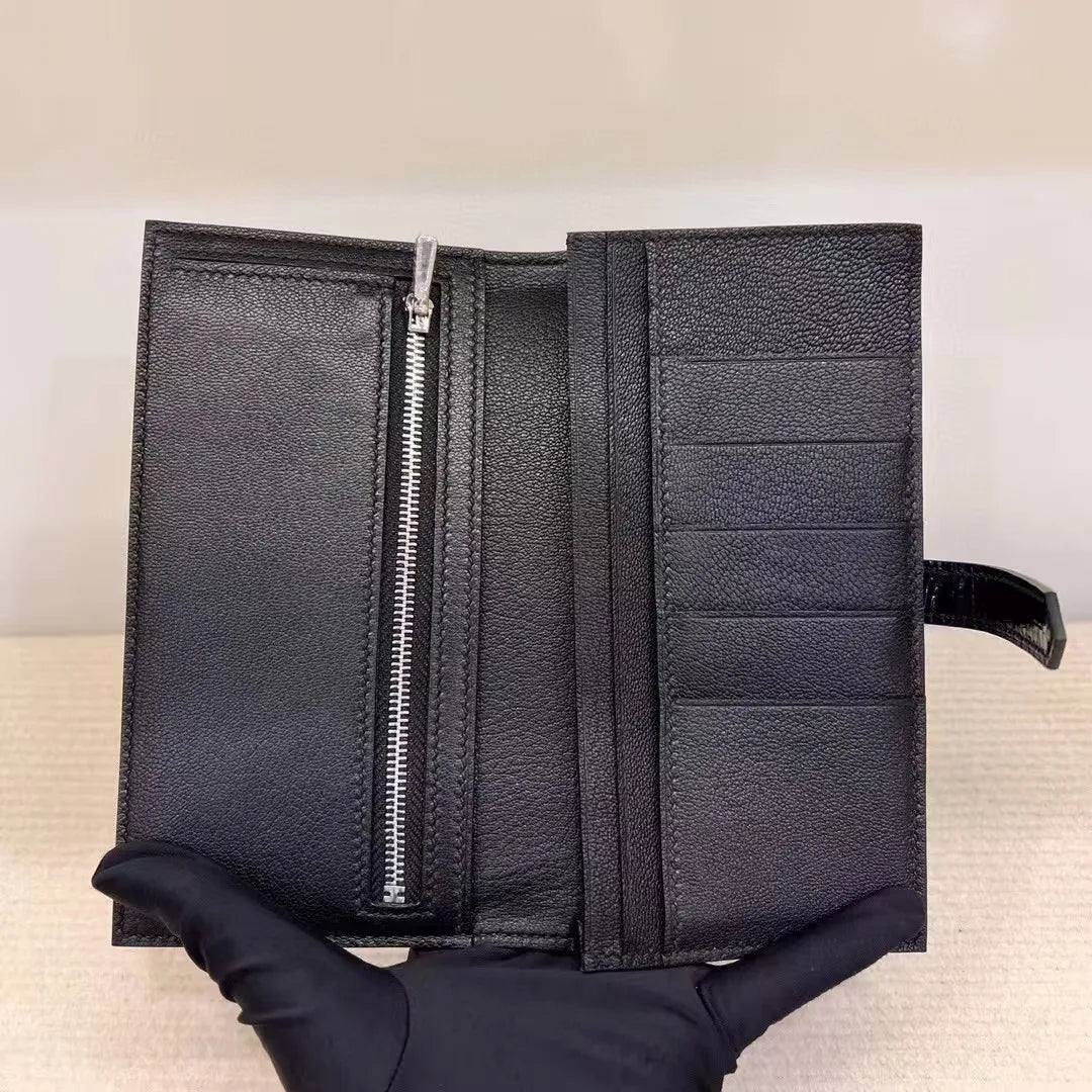 A black textured leather wallet held open by a gloved hand, showing a vertical silver zipper on the left and multiple card slots on the right.