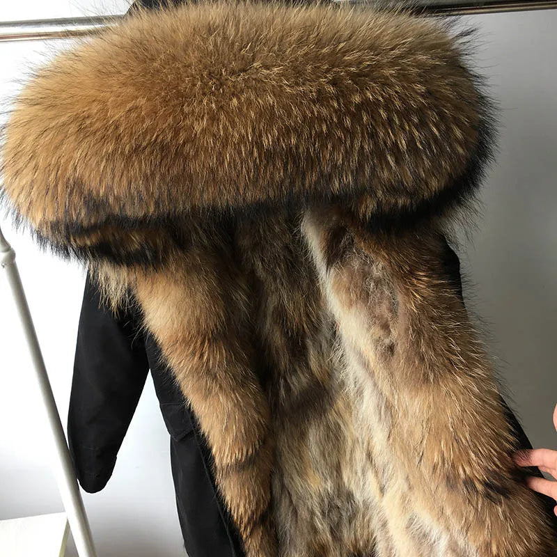A close-up of a black winter coat with a very large, luxurious brown and beige fur hood and matching faux fur trim, shown hanging on a rack.