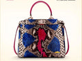 A structured handbag with a multicolor snakeskin pattern featuring blue, pink, brown, and beige tones, with magenta leather top handles and a silver-tone front clasp, set against a plain cream background.