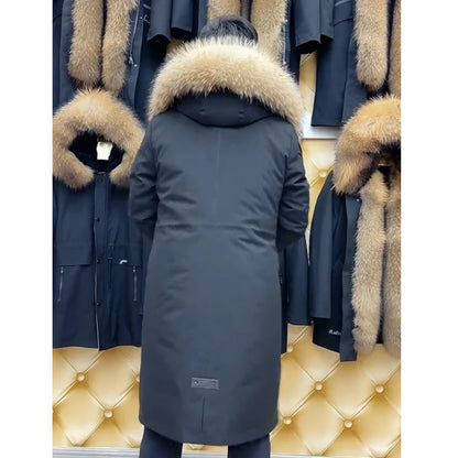 A person viewed from behind wearing a long dark gray parka with a large beige fur-trimmed hood, standing in front of a display of similar parkas on a gold tufted wall.