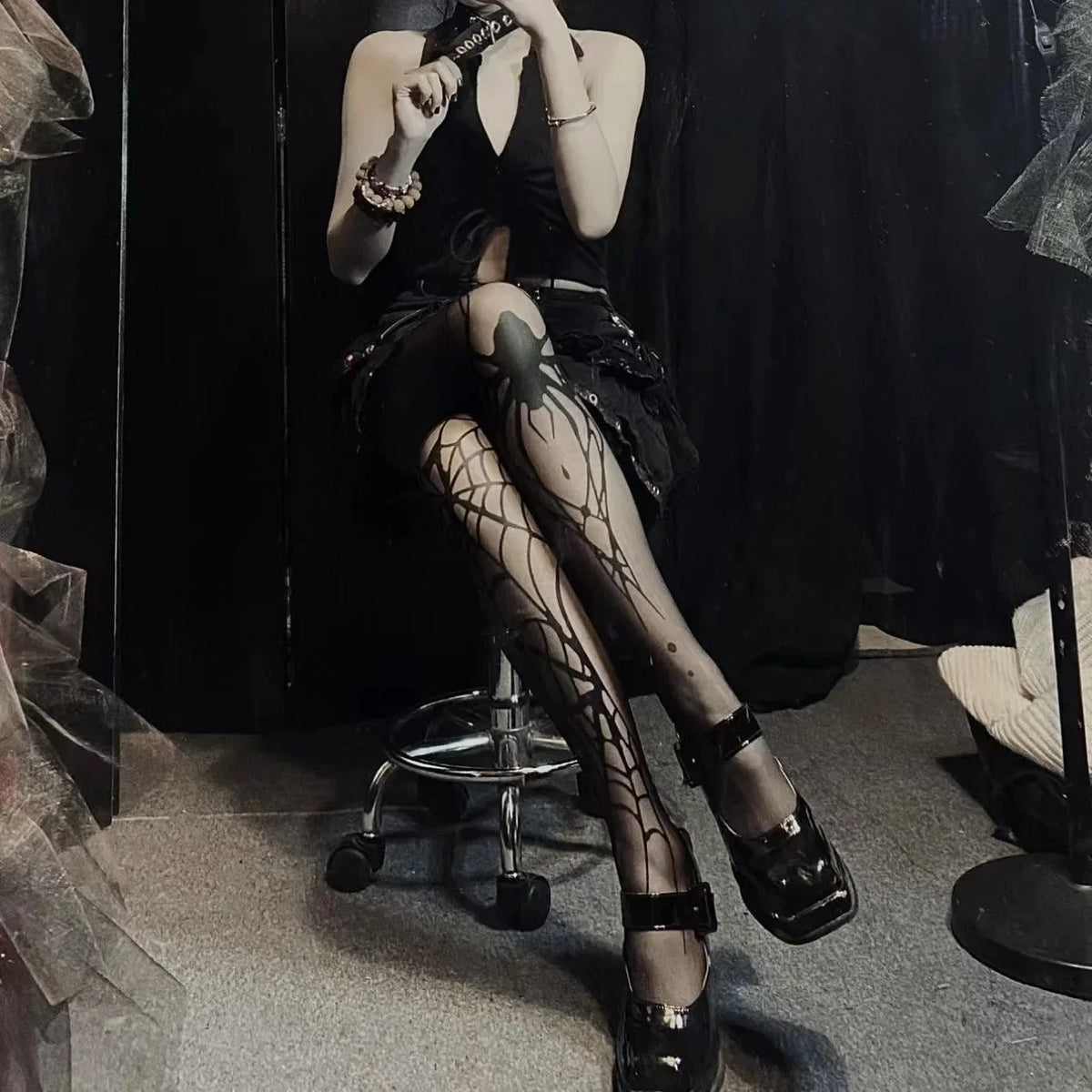 Person wearing black stockings with spider web design and black shoes in a dark room.