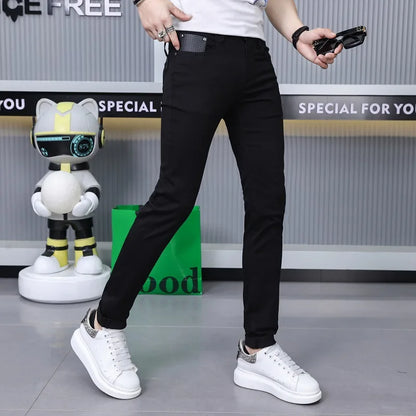 A person wearing slim black pants and white sneakers stands indoors against a gray wall with promotional text. The product being shown appears to be the pants, but because a real person and real environment are visible, the correct subject_type is Lifestyle rather than Product/Packaging.