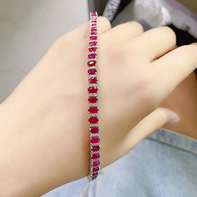 A close-up of a hand wearing a silver tennis bracelet set with oval-cut deep red gemstones.