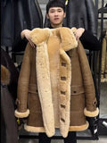 A man in a black shirt holds up a brown shearling coat with a thick cream-colored fur lining and trim. The coat features large button closures down the front and a plush collar.