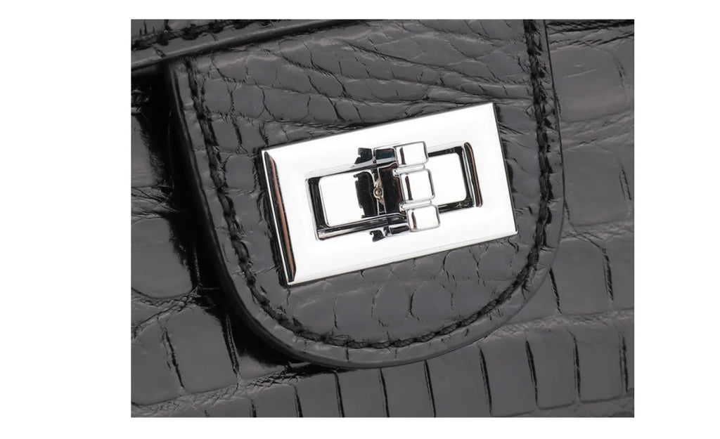Close-up of a black crocodile-embossed leather handbag featuring a polished silver-tone metal turn-lock clasp on a white background.