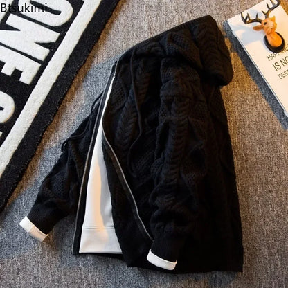 A black cable-knit zip-up hoodie jacket with a white inner lining and white cuff trims, laid flat on a gray textured carpet next to a rug and a magazine.