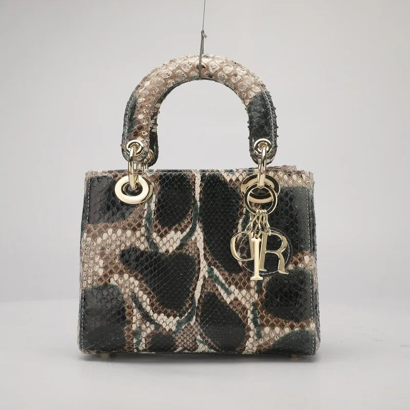 A small structured handbag with a snakeskin pattern in black, beige, and brown, featuring a top handle, gold-tone hardware, and a hanging Christian Dior CD charm.