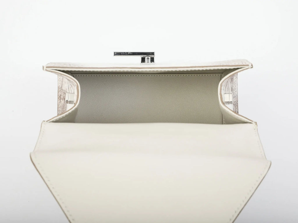 An open cream-colored leather clutch bag with a structured geometric shape, featuring a light beige interior lining and a silver-tone metal clasp at the top, set against a plain white background.