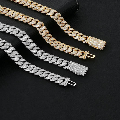 Three Cuban link chains laid diagonally on a black textured background, with one gold chain, one silver chain, and one mixed gold-and-silver chain. The links are covered in small clear stones, and the clasps are also stone-covered.