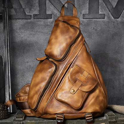A distressed brown leather duffel-style backpack with multiple zippered compartments and a front pocket, displayed on a rustic wooden surface against a dark textured wall.