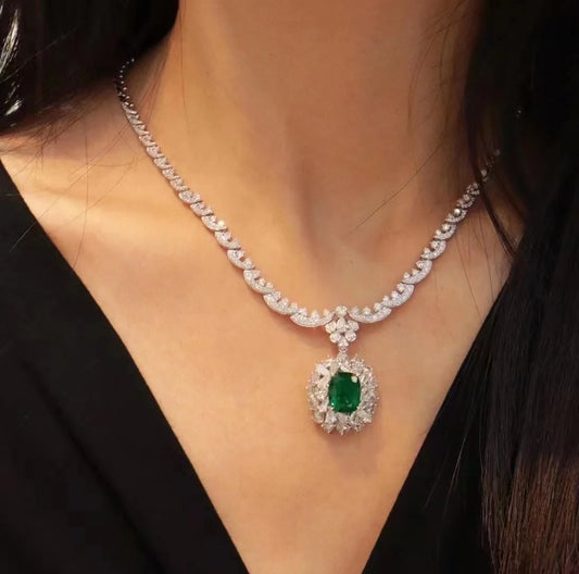 Elegant diamond necklace with a green gemstone on a person wearing a black top.