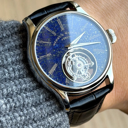 Luxury watch with blue face and black leather strap worn on a wrist.