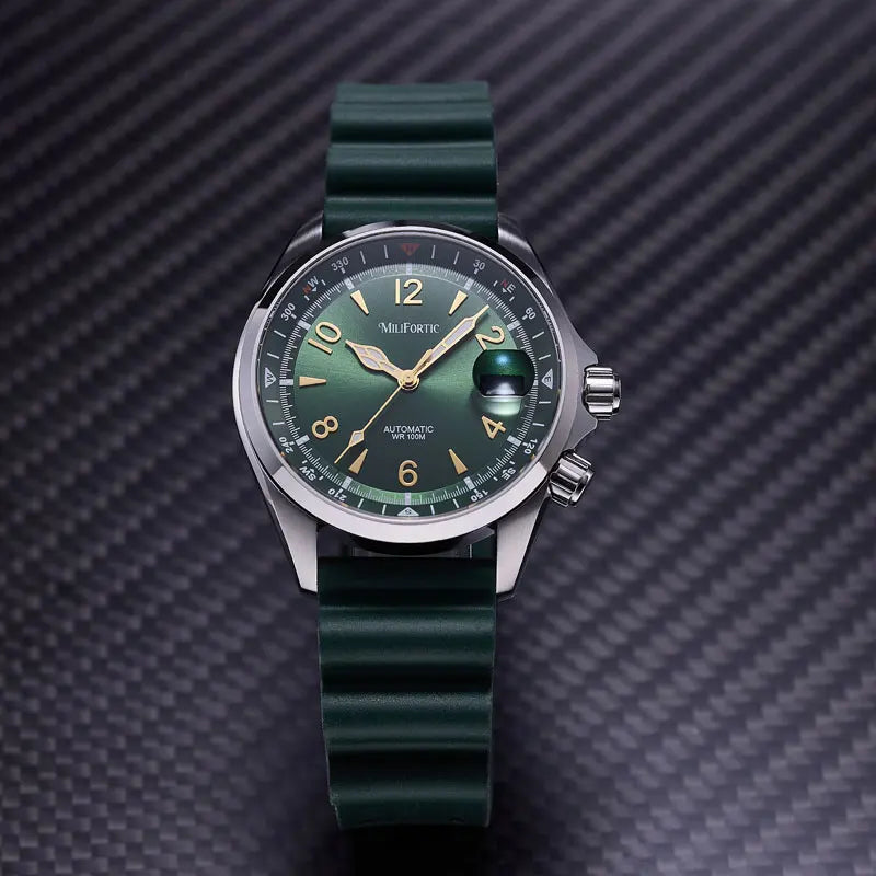 A Mil-Fortis automatic watch with a dark green dial and a matching dark green silicone strap, displayed on a textured dark gray carbon fiber background.