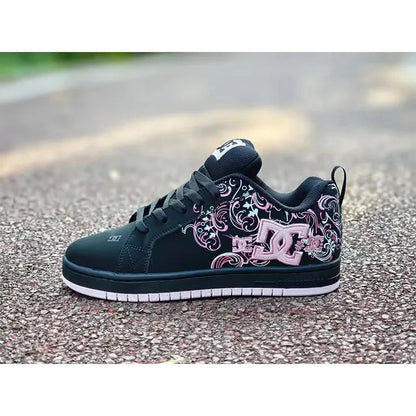 A black DC skate shoe with pink and white floral scrollwork and a large DC logo on the side, photographed outdoors on a paved surface.