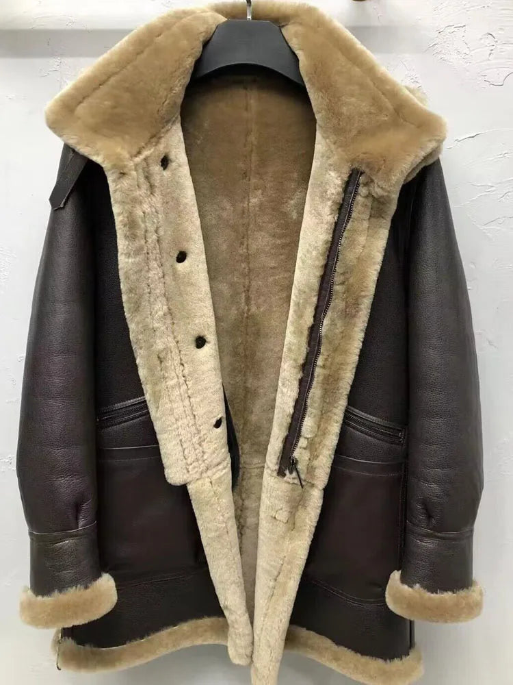 A dark brown leather aviator-style jacket with thick beige shearling lining, featuring a large collar, button closure, and zippered front, hanging on a black hanger against a white wall.