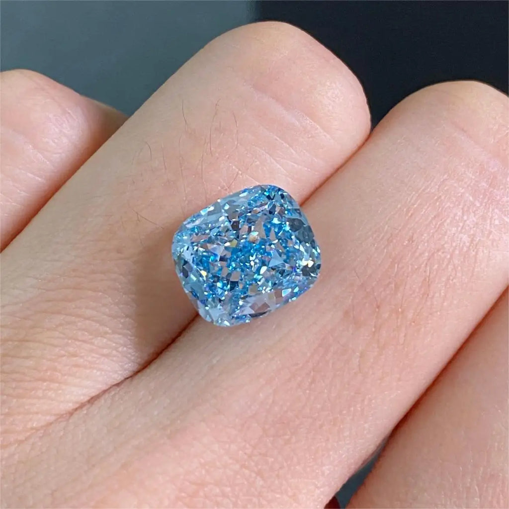 A loose cushion-cut light blue gemstone displayed on a person's finger against a dark gray background.