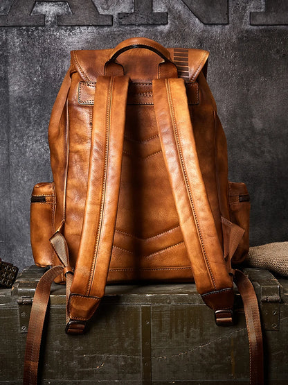 A brown leather backpack shown from the back, resting on a dark wooden crate against a textured gray wall.