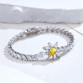 A silver-toned tennis bracelet featuring a central flower motif with a bright yellow oval center stone and surrounding clear marquise and round stones, displayed on a white surface.