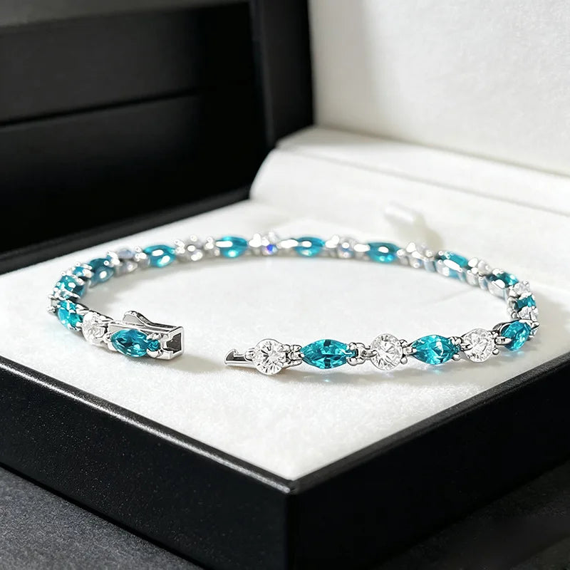 A silver cuff bracelet with marquise-cut turquoise blue crystals and clear round crystals, displayed inside an open black jewelry box with a white velvet lining.