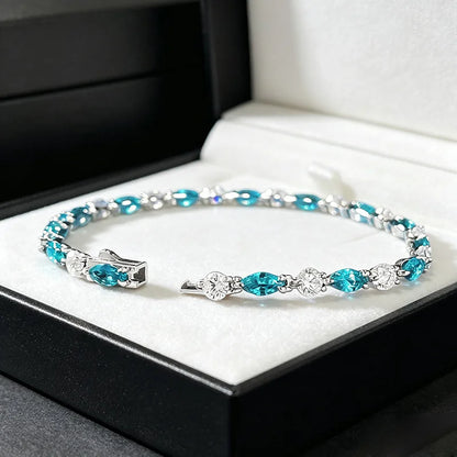 A silver cuff bracelet with marquise-cut turquoise blue crystals and clear round crystals, displayed inside an open black jewelry box with a white velvet lining.