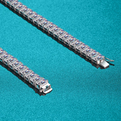 A close-up studio shot of a silver tennis bracelet with rectangular blue gemstones, shown in two parallel diagonal segments on a textured turquoise background.