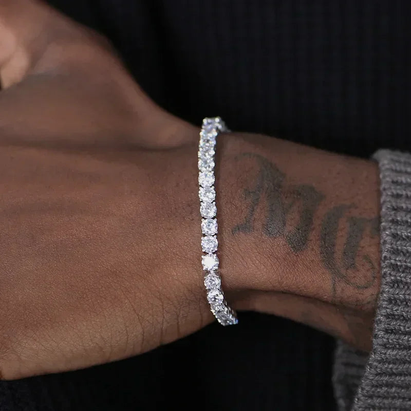 A close-up of a person's wrist wearing a sparkling silver-toned tennis bracelet with clear stones, set against a dark background.
