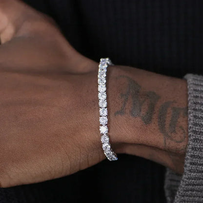 A close-up of a person's wrist wearing a sparkling silver-toned tennis bracelet with clear stones, set against a dark background.