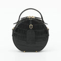 A black crocodile-embossed leather handbag with a top handle, gold-tone hardware, and a front hanging tag, photographed on a clean white background.