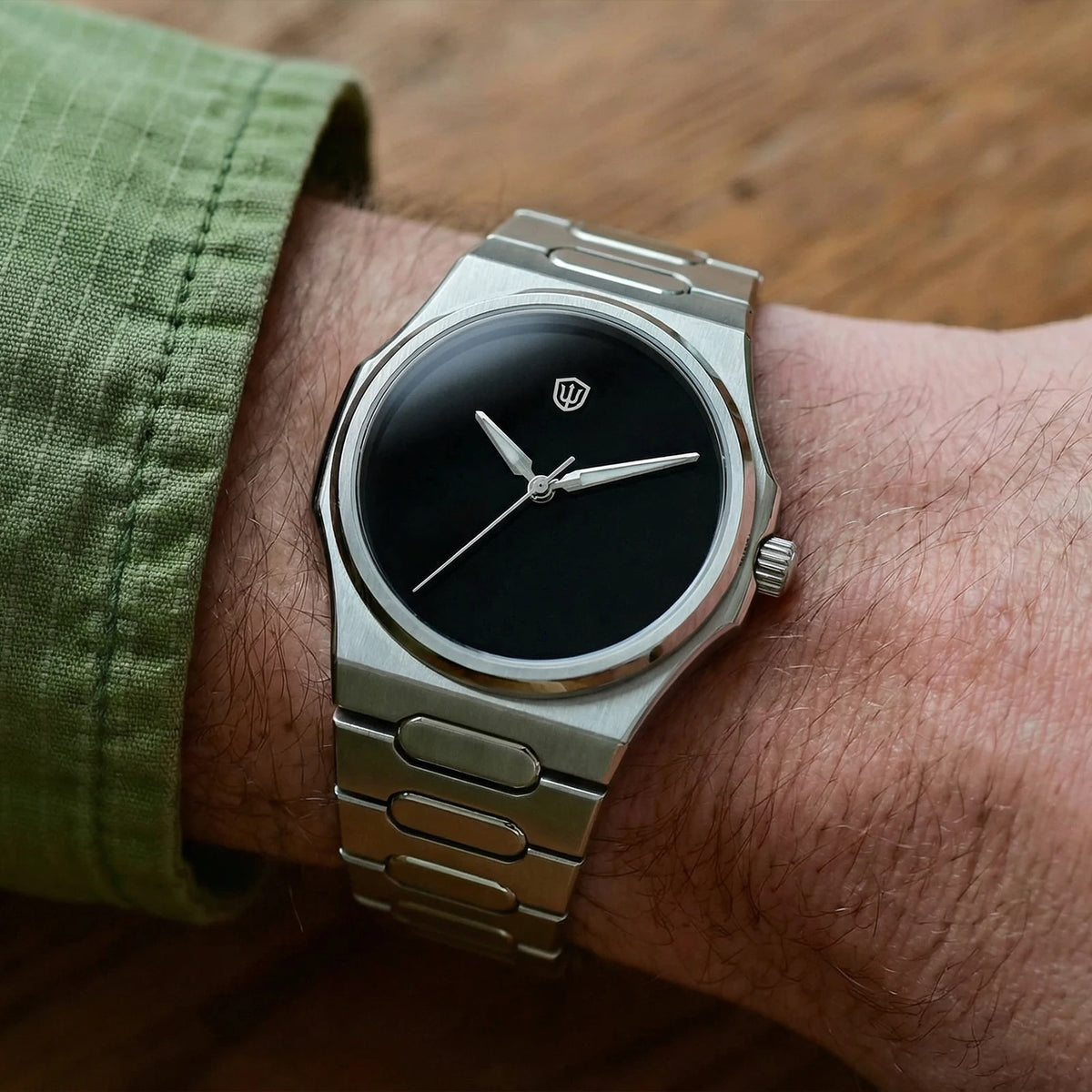 Silver watch with black dial on a wrist, green sleeve visible