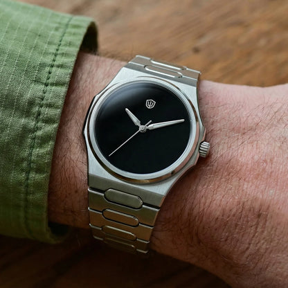 Silver watch with black dial on a wrist, green sleeve visible