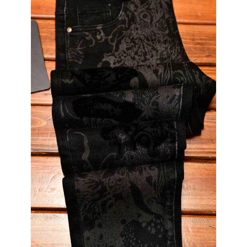 Black patterned jeans with a dark gray and black floral jacquard design, folded on a wooden surface.