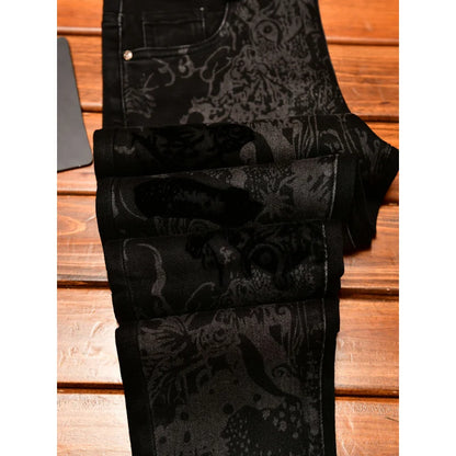 Black patterned jeans with a dark gray and black floral jacquard design, folded on a wooden surface.