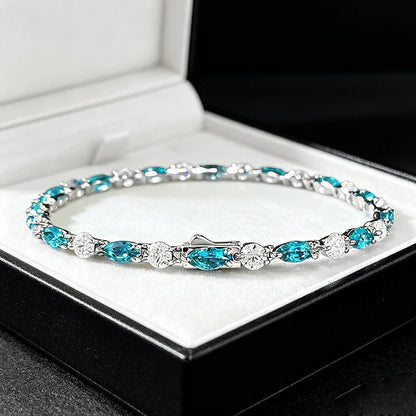 A silver tennis bracelet with vibrant turquoise blue marquise and oval gemstones, displayed inside an open black jewelry box with a white velvet lining.