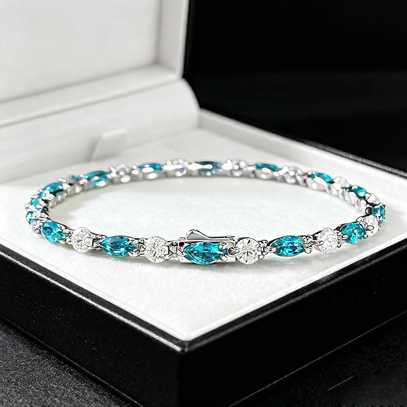 A silver tennis bracelet with vibrant turquoise blue marquise and oval gemstones, displayed inside an open black jewelry box with a white velvet lining.