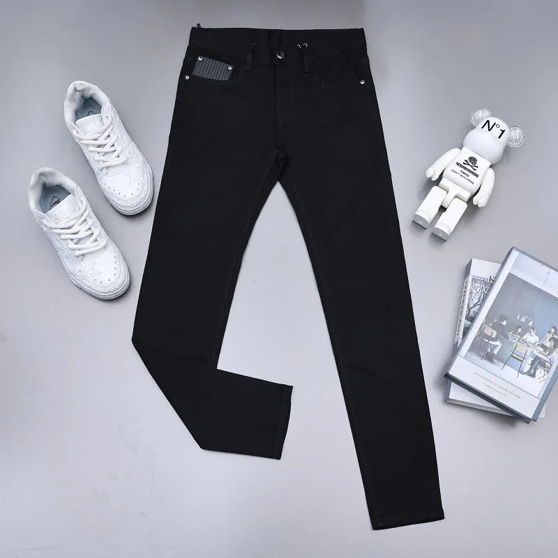 Black slim-fit jeans laid flat on a light gray surface, styled with white sneakers, a white bear figure, and a stack of magazines.