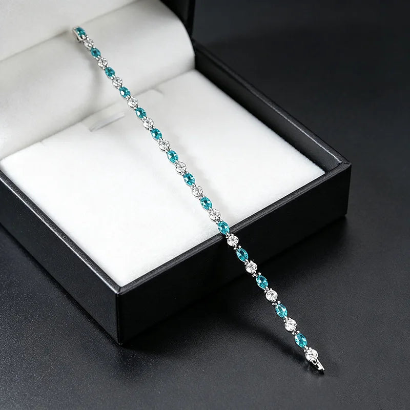 A silver tennis bracelet with alternating turquoise and clear cubic zirconia stones, displayed diagonally across an open black jewelry box with a white cushion.