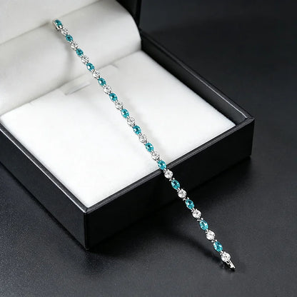 A silver tennis bracelet with alternating turquoise and clear cubic zirconia stones, displayed diagonally across an open black jewelry box with a white cushion.