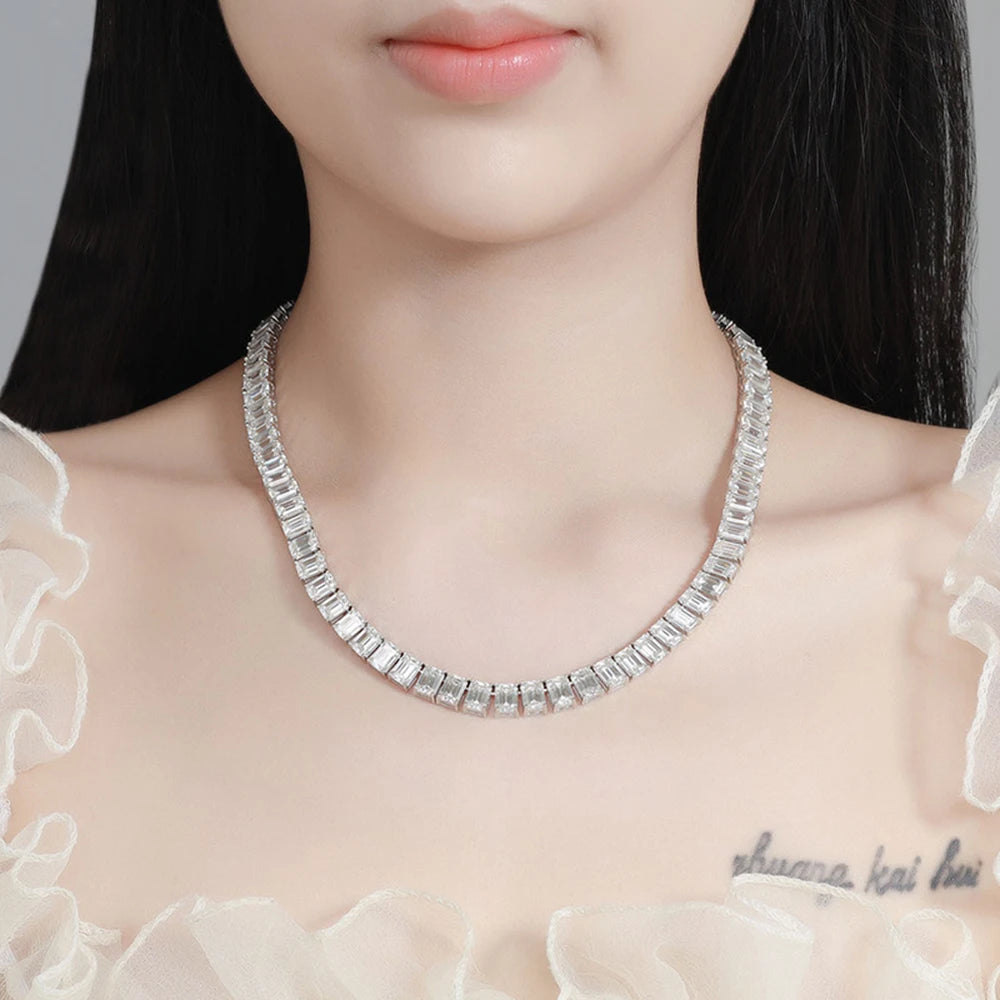 A close-up of a model wearing a silver-toned rectangular-link necklace with clear stones, styled with a sheer white ruffled top.