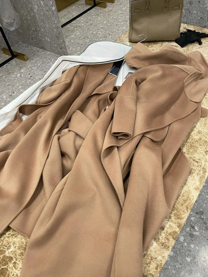 A draped camel-colored wool coat or blazer laid out on a marble surface, with a white hanger and a beige handbag nearby.