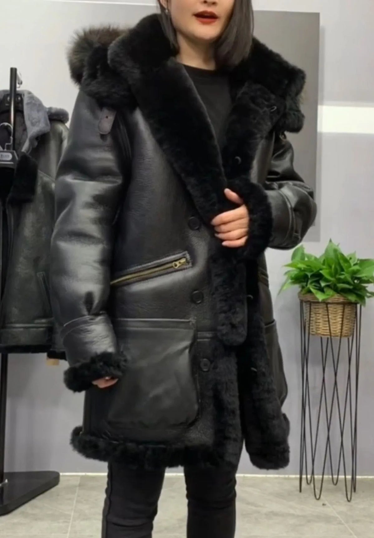 A woman wearing a black shearling-lined aviator-style jacket with a large dark fur collar, standing in a store interior.
