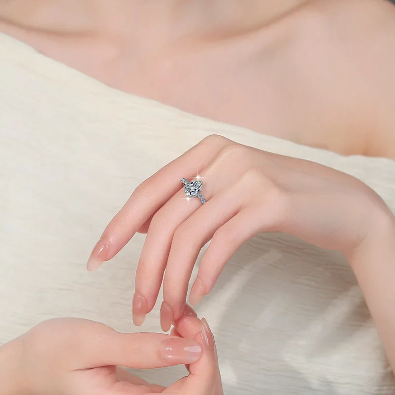 A close-up of a hand wearing a silver-toned ring with a sparkling clear gemstone, resting on soft cream fabric.