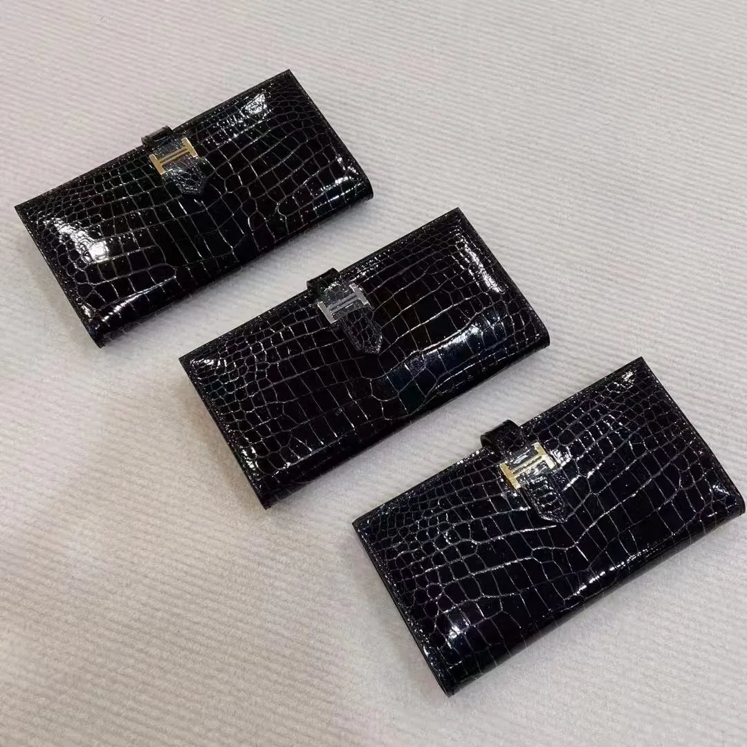 Three black crocodile-embossed leather bifold wallets arranged diagonally on a textured off-white fabric background.