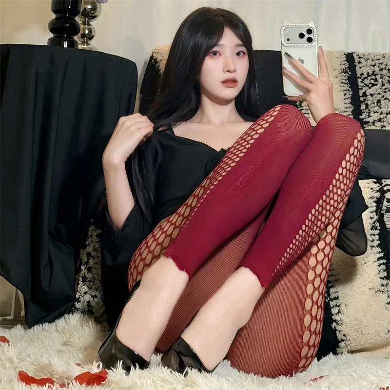 Woman sitting on a couch wearing red fishnet stockings and a black top.