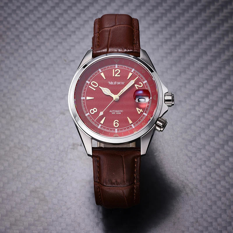 A wristwatch with a silver-toned metal case, a red dial, and a brown leather strap, photographed on a textured gray background.