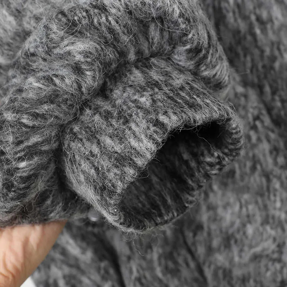 Close-up of a thick, fuzzy gray knit fabric sleeve being held by a hand, showing the soft texture and ribbed cuff detail.
