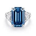 A halo-style moissanite ring featuring a large rectangular blue moissanite center stone with two clear accent stones on either side, set in a silver-colored metal band. The brand logo 'Plc HOLYCOME' is visible in the top left corner.