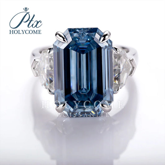 A halo-style moissanite ring featuring a large rectangular blue moissanite center stone with two clear accent stones on either side, set in a silver-colored metal band. The brand logo 'Plc HOLYCOME' is visible in the top left corner.