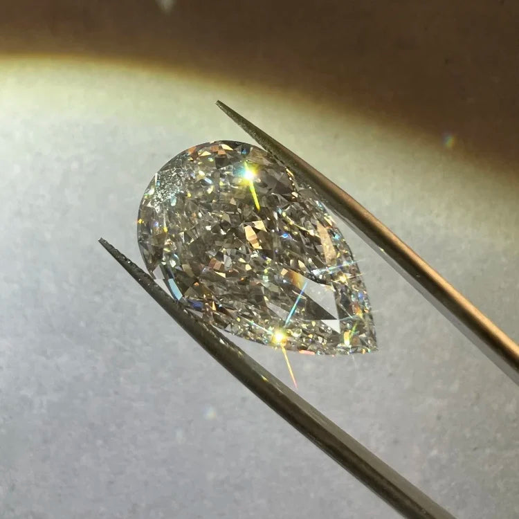 A pear-cut diamond held between metal tweezers against a softly lit neutral background.