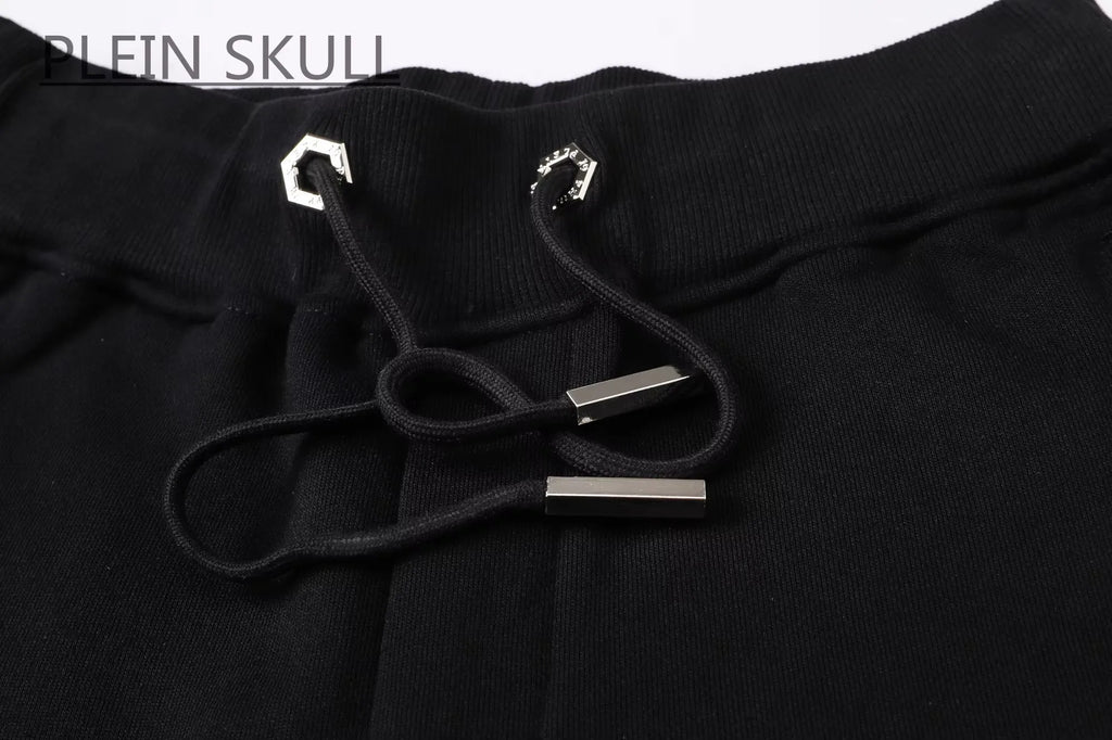 Close-up of black sweatpants with a black drawstring and silver metal accents, featuring the text 'PLEIN SKULL' in the top left corner.