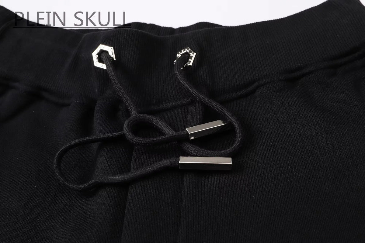 Close-up of black sweatpants with a black drawstring and silver metal accents, featuring the text 'PLEIN SKULL' in the top left corner.